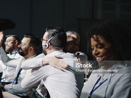 People in headsets looking elated and hugging.